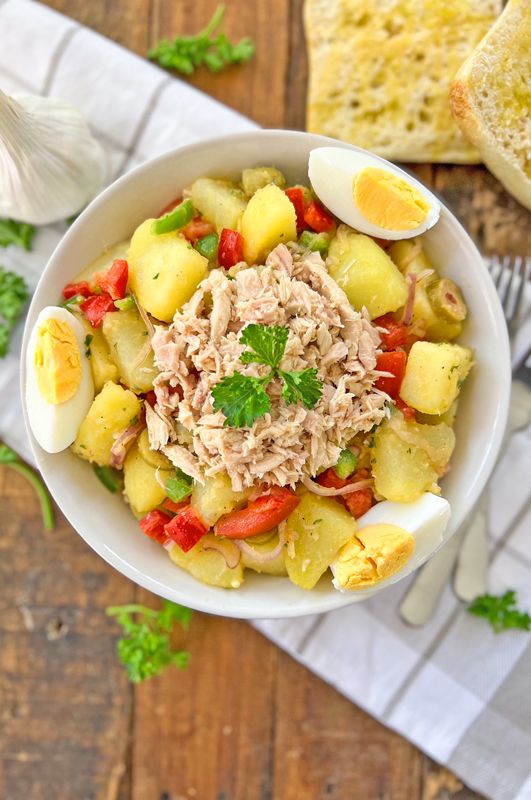 a white bowl filled with tuna and pineapple salad next to bread on a wooden table