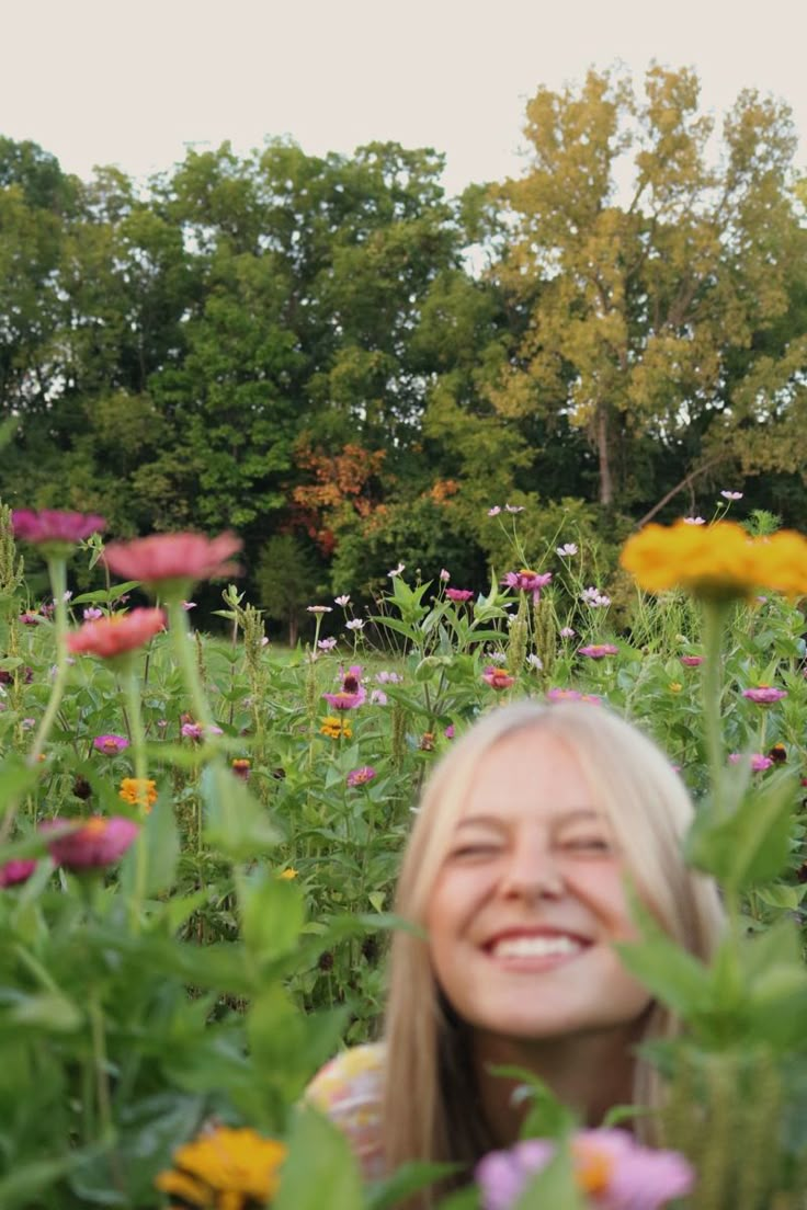 a woman standing in the middle of a field full of flowers smiling at the camera