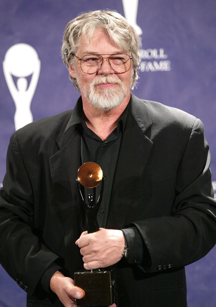 an older man holding a trophy in his right hand and looking at the camera while wearing a black suit