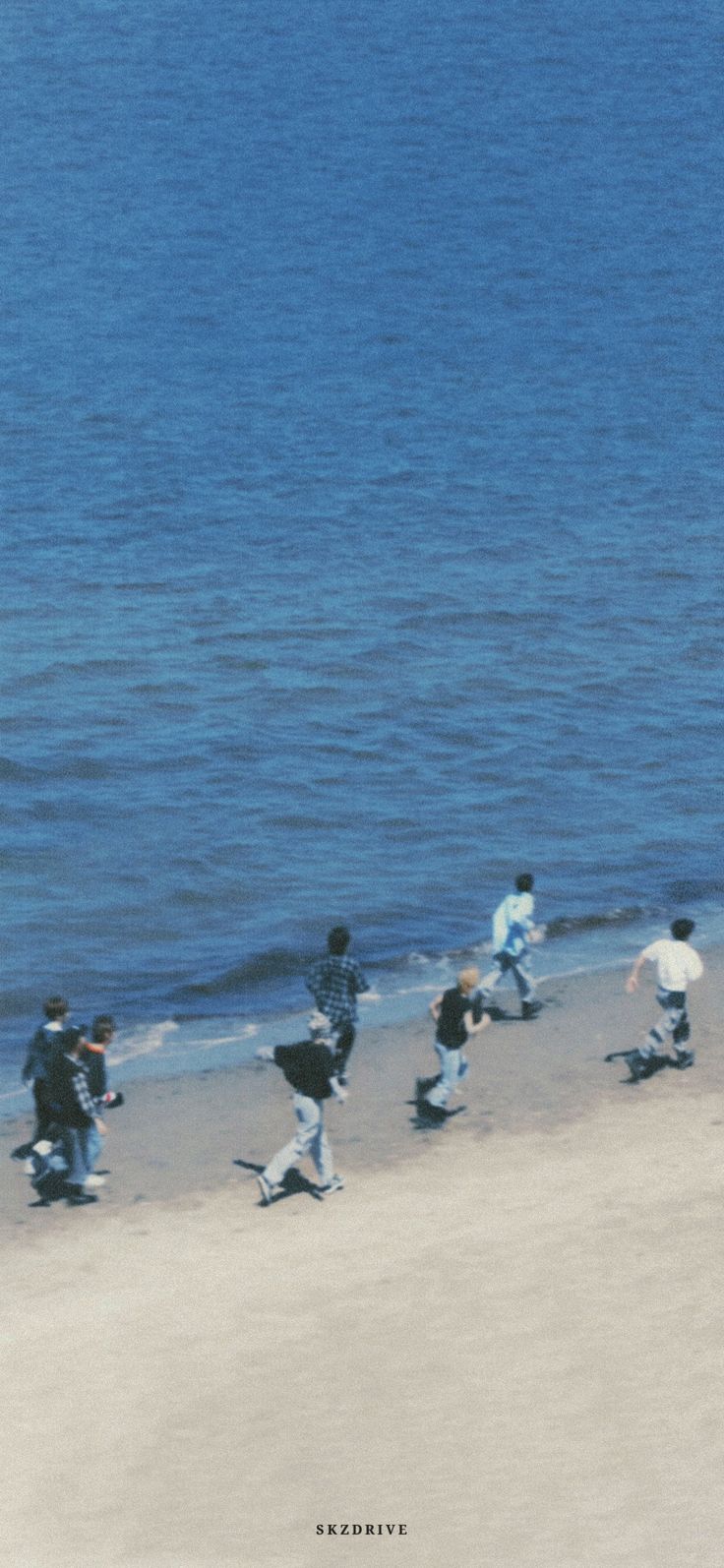 a group of people running on the beach next to the ocean with water in the background