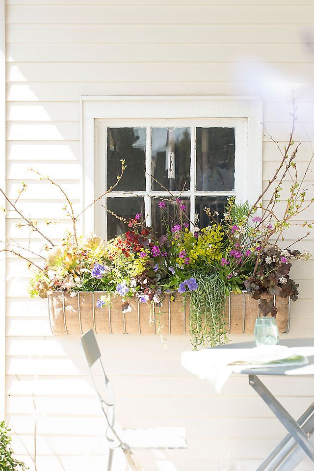 a window box filled with lots of flowers next to a table and two chairs outside