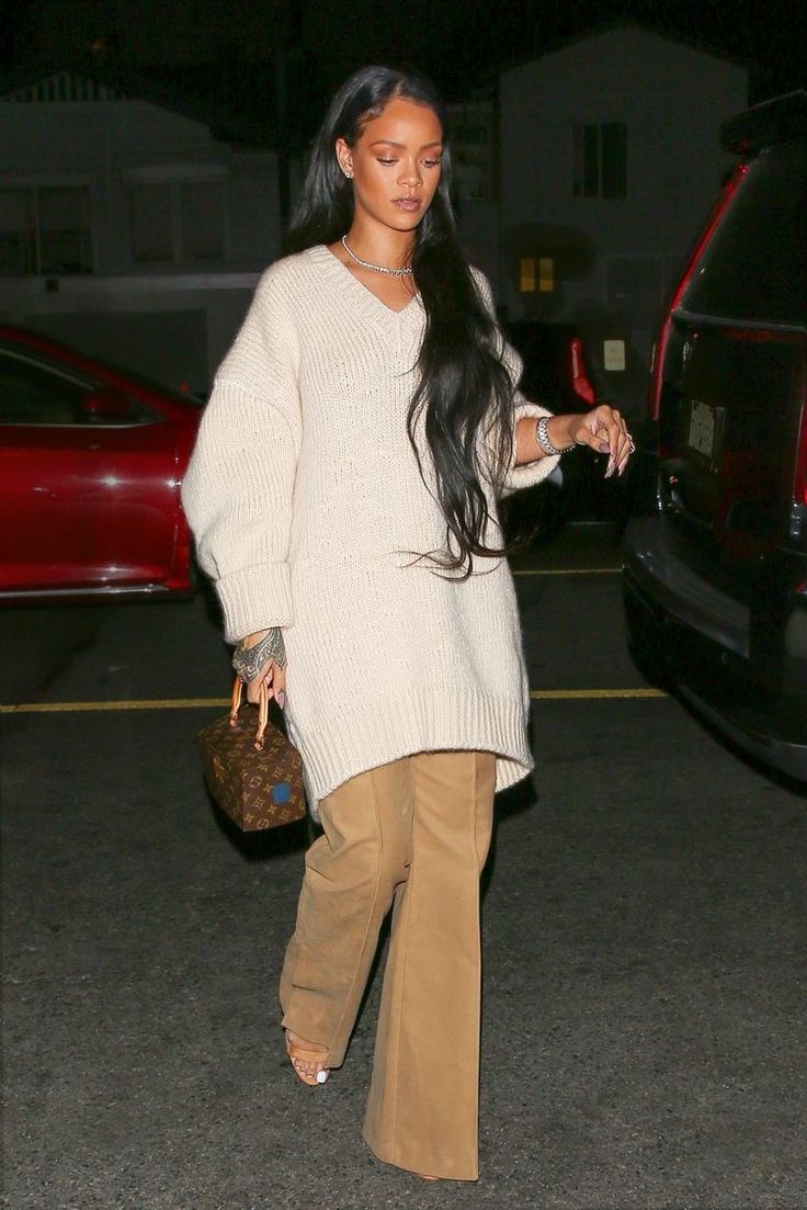 a woman with long black hair wearing brown pants and a white sweater is walking down the street