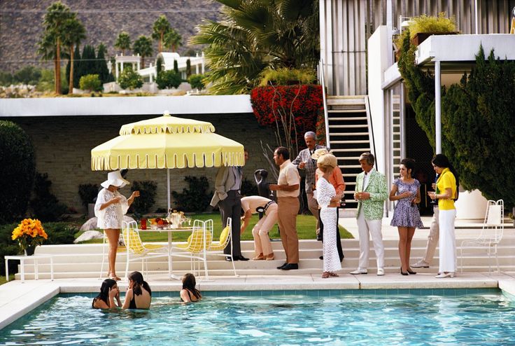 people are standing around in the pool near an open air swimming area with yellow and white umbrellas