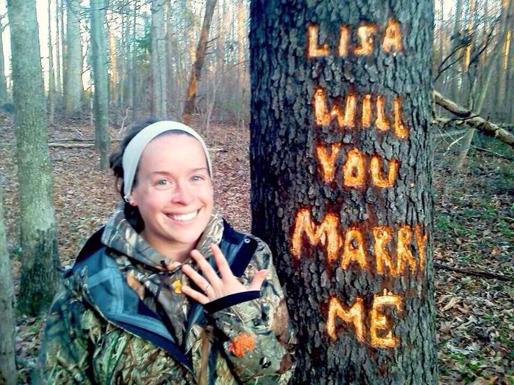 a woman standing next to a tree with writing written on it in orange ink that says, i will you marry me