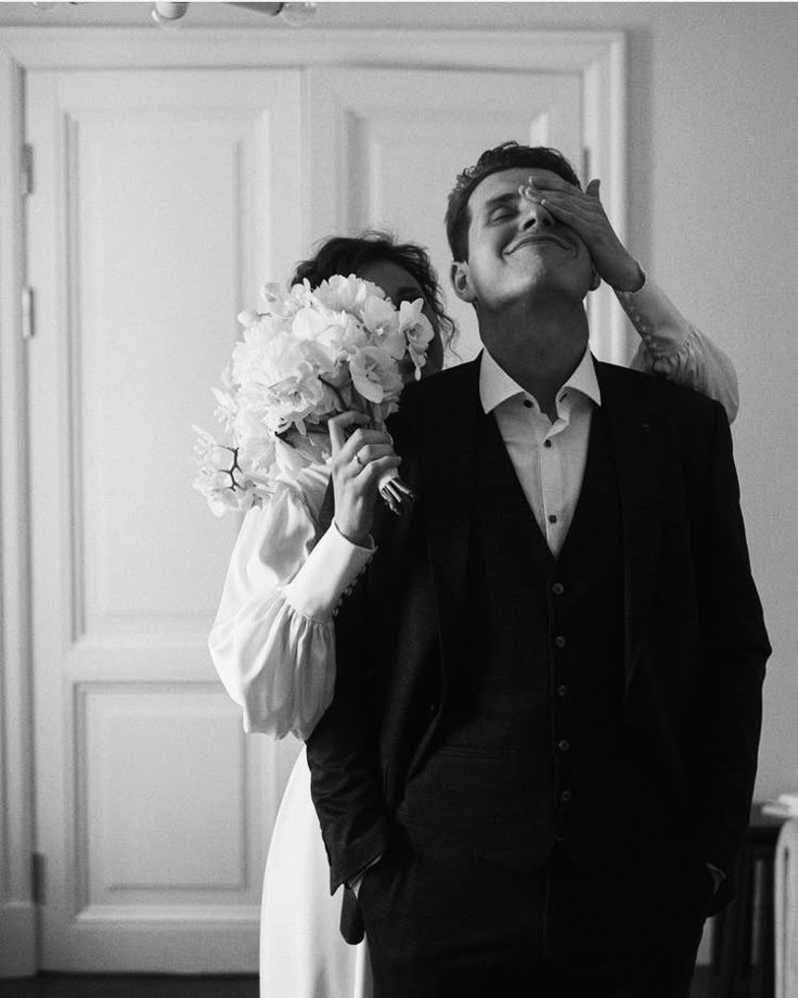 a man and woman standing next to each other in front of a door holding flowers