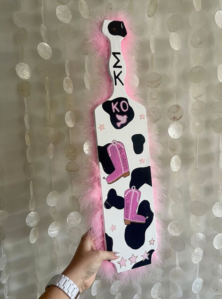 a hand holding up a bottle shaped like a cow with pink fur around the neck