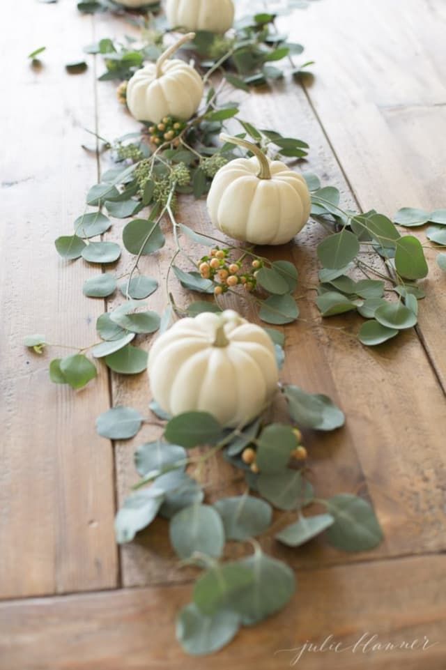 white pumpkins and greenery are arranged on the floor for a long table runner