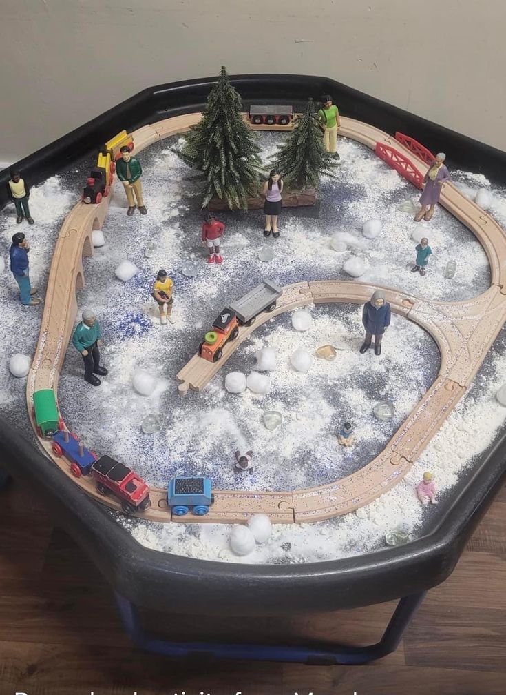 a toy train set sitting on top of a wooden table covered in snow and toys