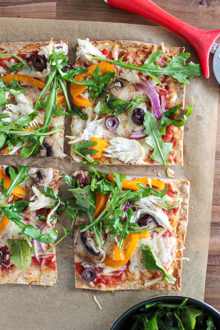 four square pizzas with various toppings on top of a cutting board next to a bowl of salad