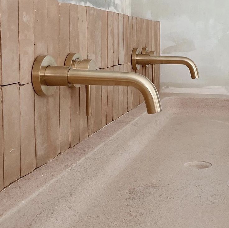 two brass faucets on the side of a bathroom wall