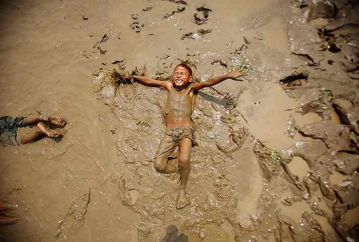 two people are in the mud and one person is laying on his back with their arms spread out