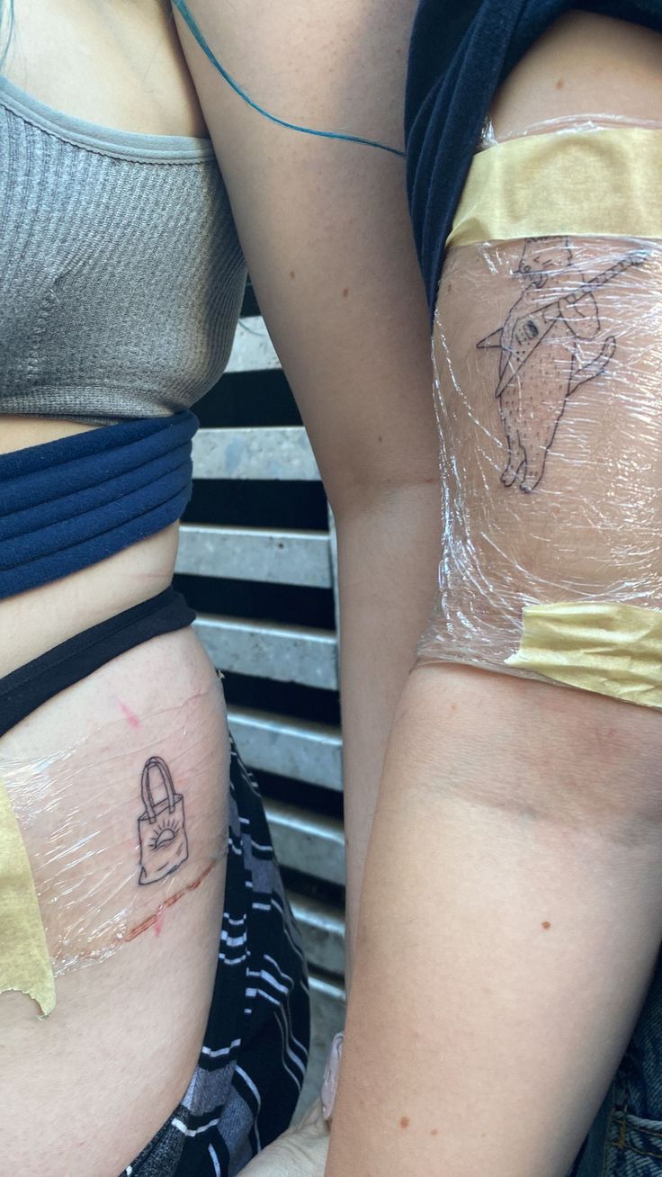 two women with tattoos on their butts and one has a bag on her stomach