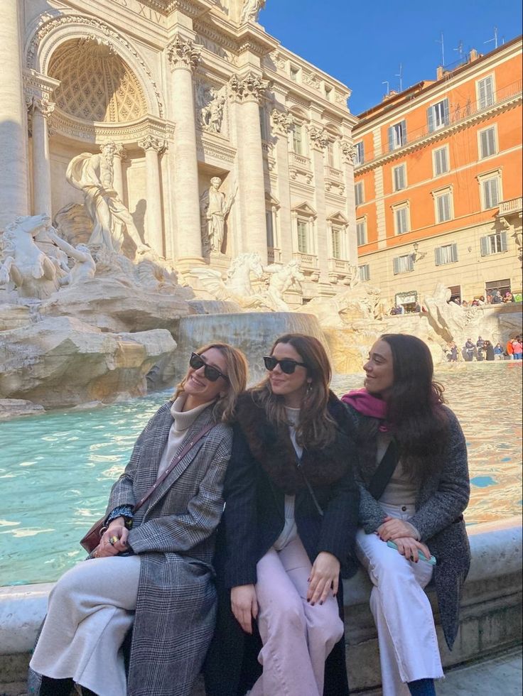 three women sitting next to each other in front of a fountain