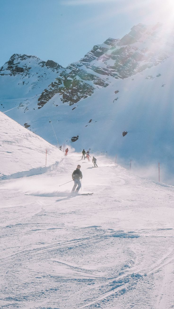 skiers skiing down a snowy mountain slope on a sunny day with the sun shining