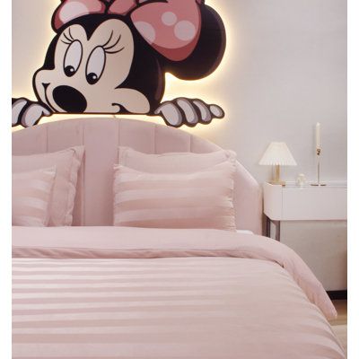 a bed with pink comforter and mickey mouse head on the wall next to it