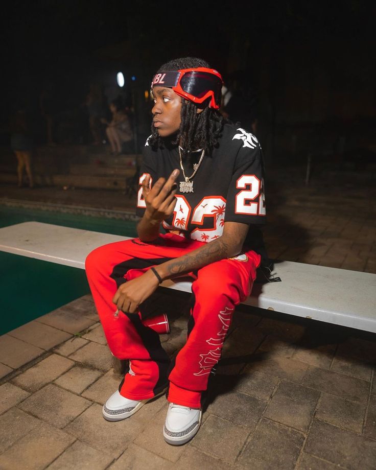 a man sitting on top of a white bench wearing red pants and a black shirt