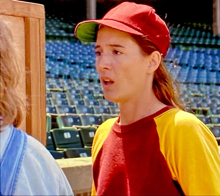 a woman in a red and yellow baseball cap talking to someone on the sidelines