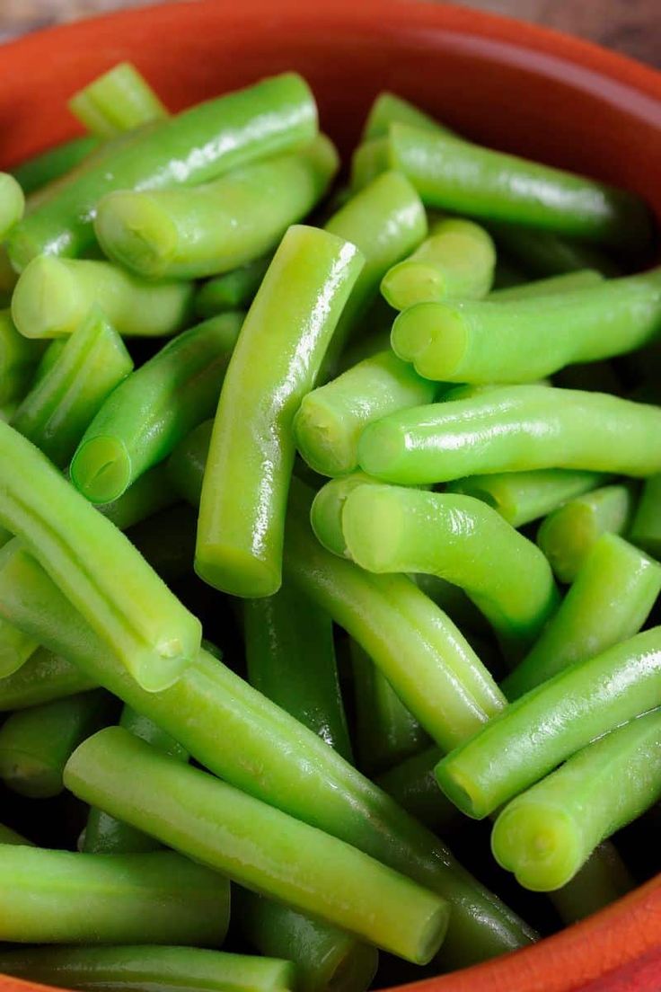 a bowl filled with green beans on top of a wooden table