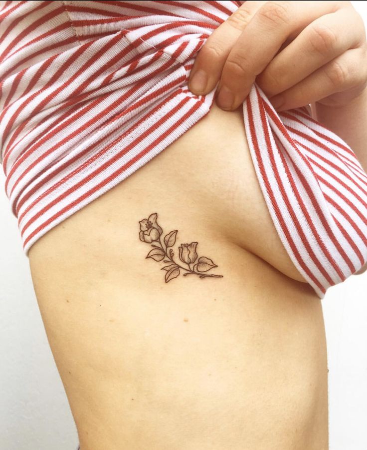 a woman's stomach with a small flower tattoo on her left side ribcage