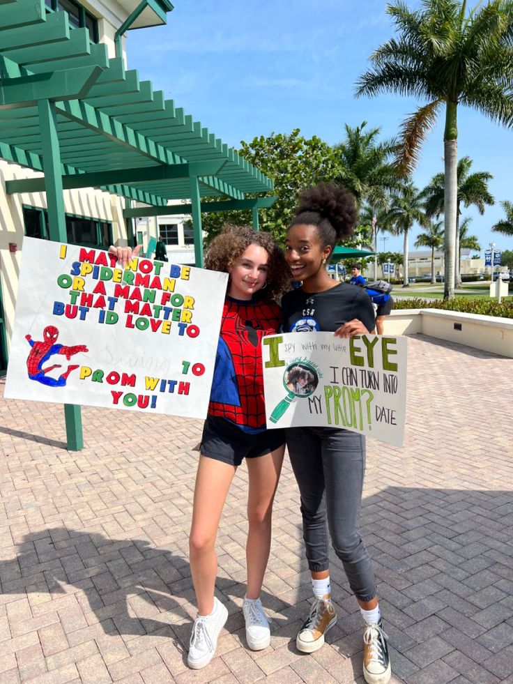 two young women holding up signs in front of a green and white building with palm trees