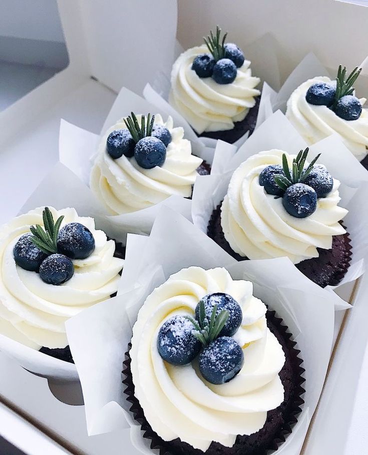 four cupcakes with white frosting and blueberries on top in a box