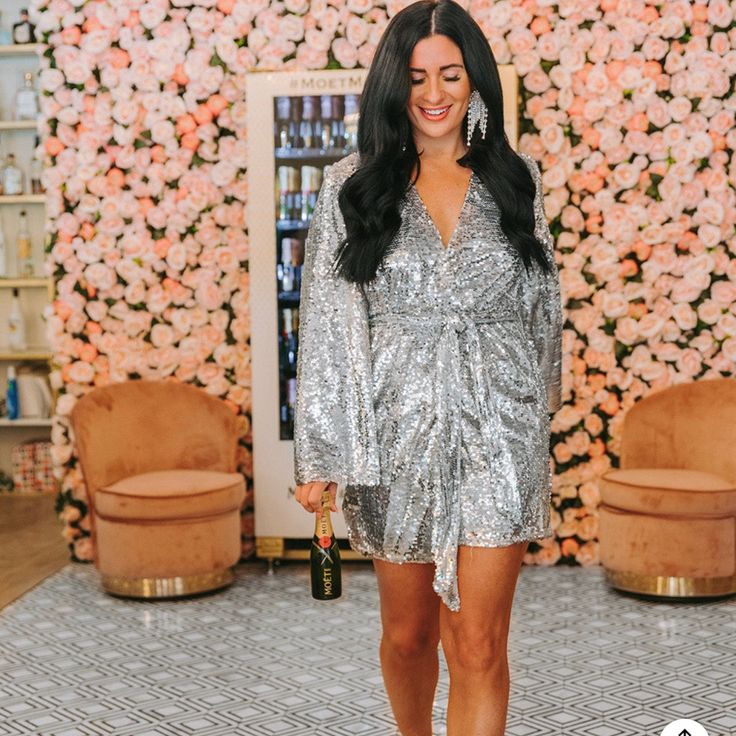 a woman standing in front of a flower wall wearing a silver sequin dress and heels