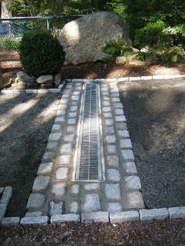 a brick walkway in the middle of a graveled area next to trees and rocks