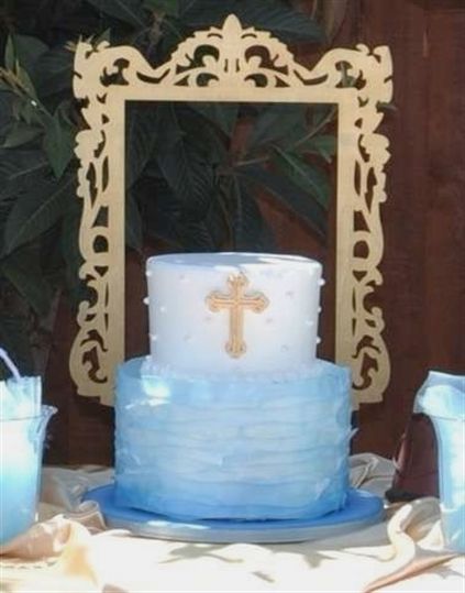 a blue and white wedding cake with a cross on the top sits in front of a gold frame