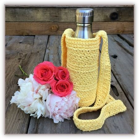 a crocheted yellow water bottle and flowers on a wooden table with wood planks