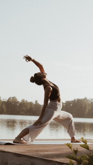 a man is doing yoga on a dock by the water with his hands in the air