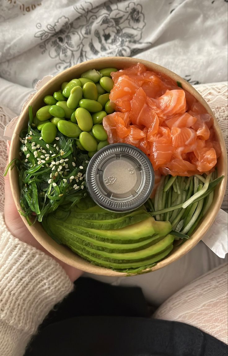 a person holding a bowl filled with different types of vegetables and fish on top of it