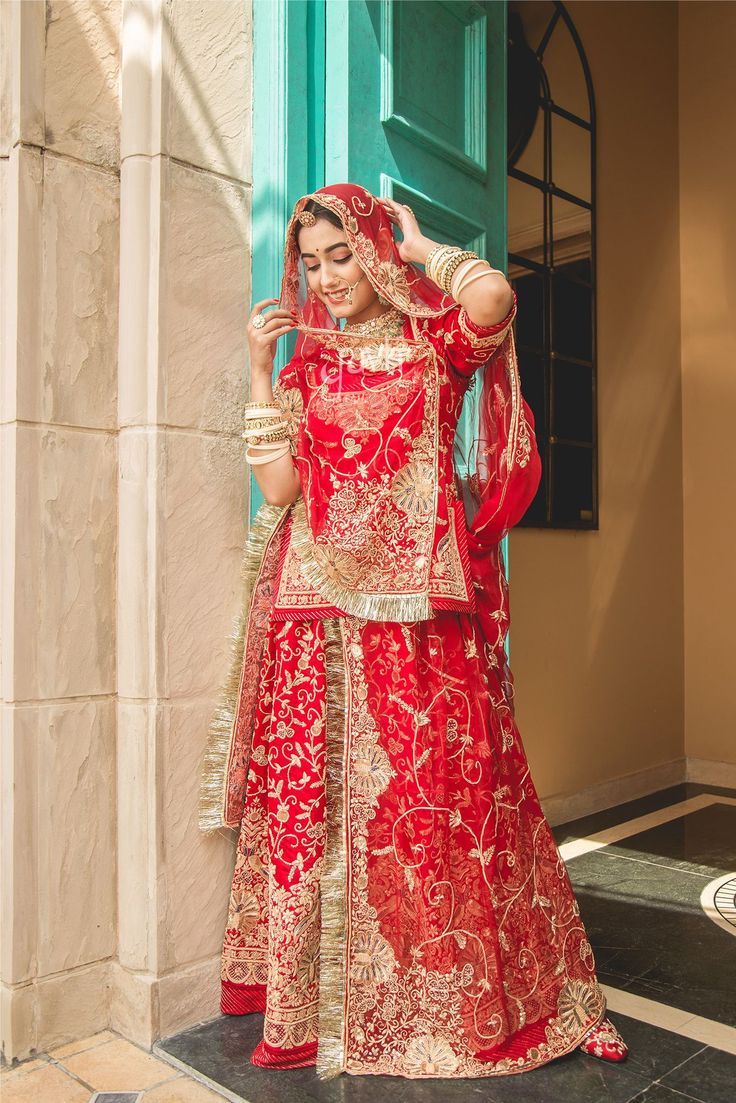 a woman in a red and gold bridal outfit stands outside the door of a building