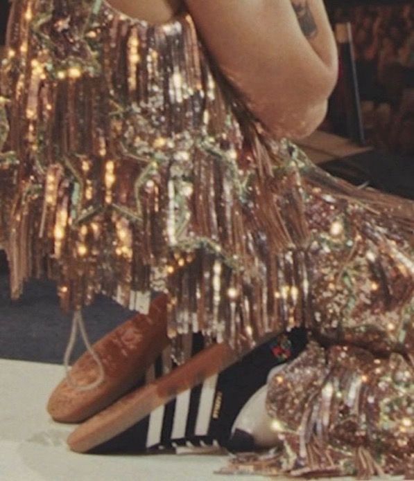 a woman in a gold dress is sitting on the floor with her legs crossed and hands behind her head