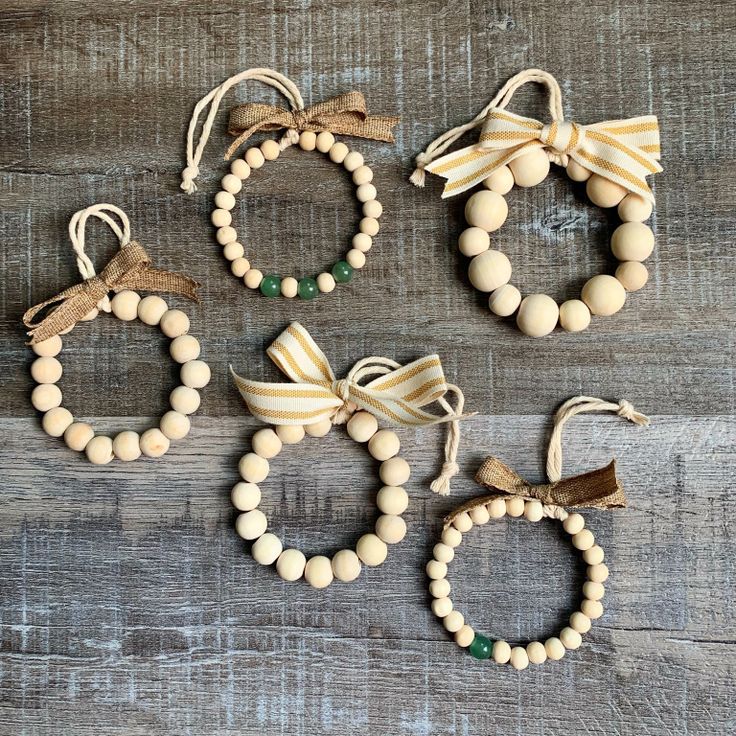 four bracelets with wooden beads and bows hanging from strings on a wood surface,