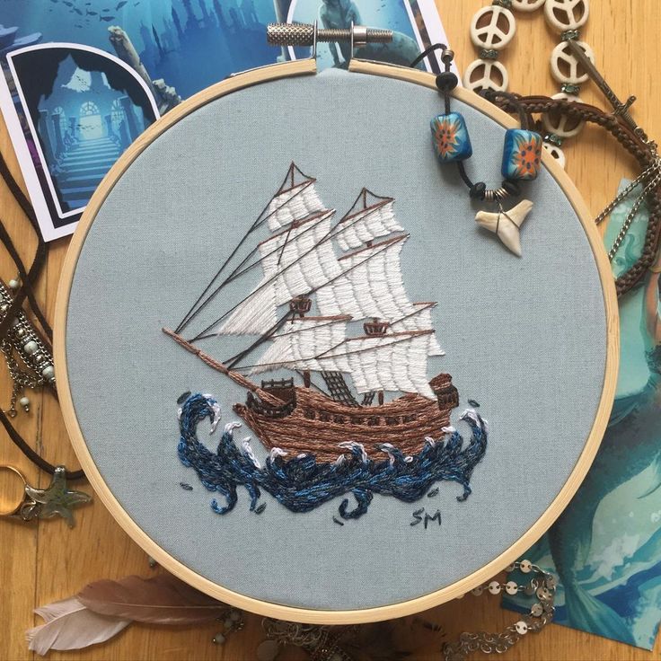 an embroidered sailboat is shown on a wooden table with other items and pictures around it