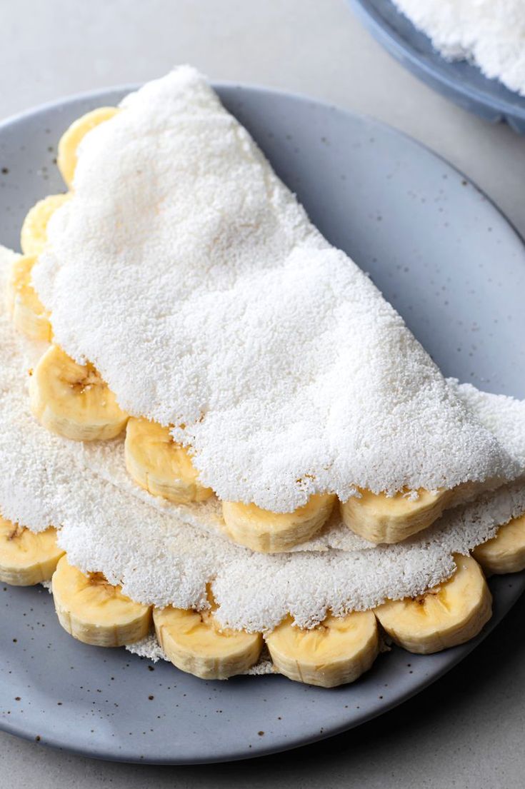 bananas and powdered sugar are stacked on a plate with two bowls in the background