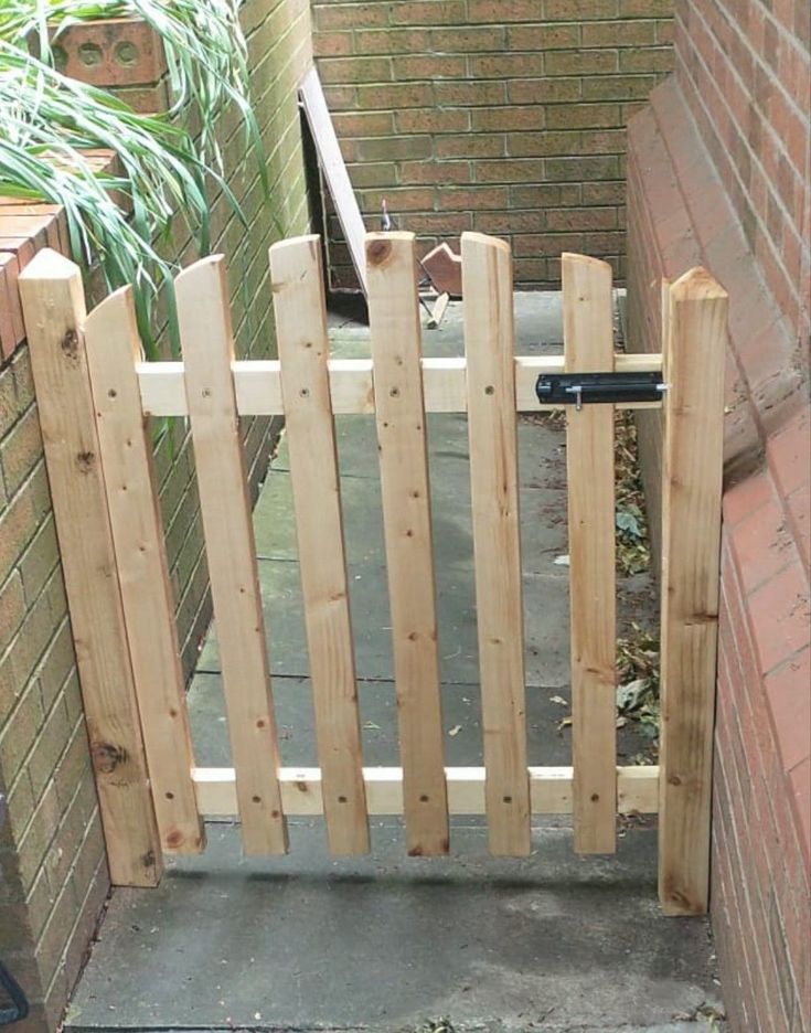 an open wooden gate on the side of a brick building next to a planter