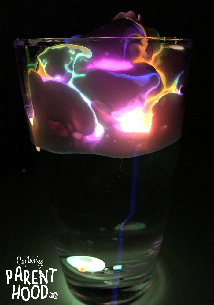 a glass filled with liquid sitting on top of a black table next to a lit candle