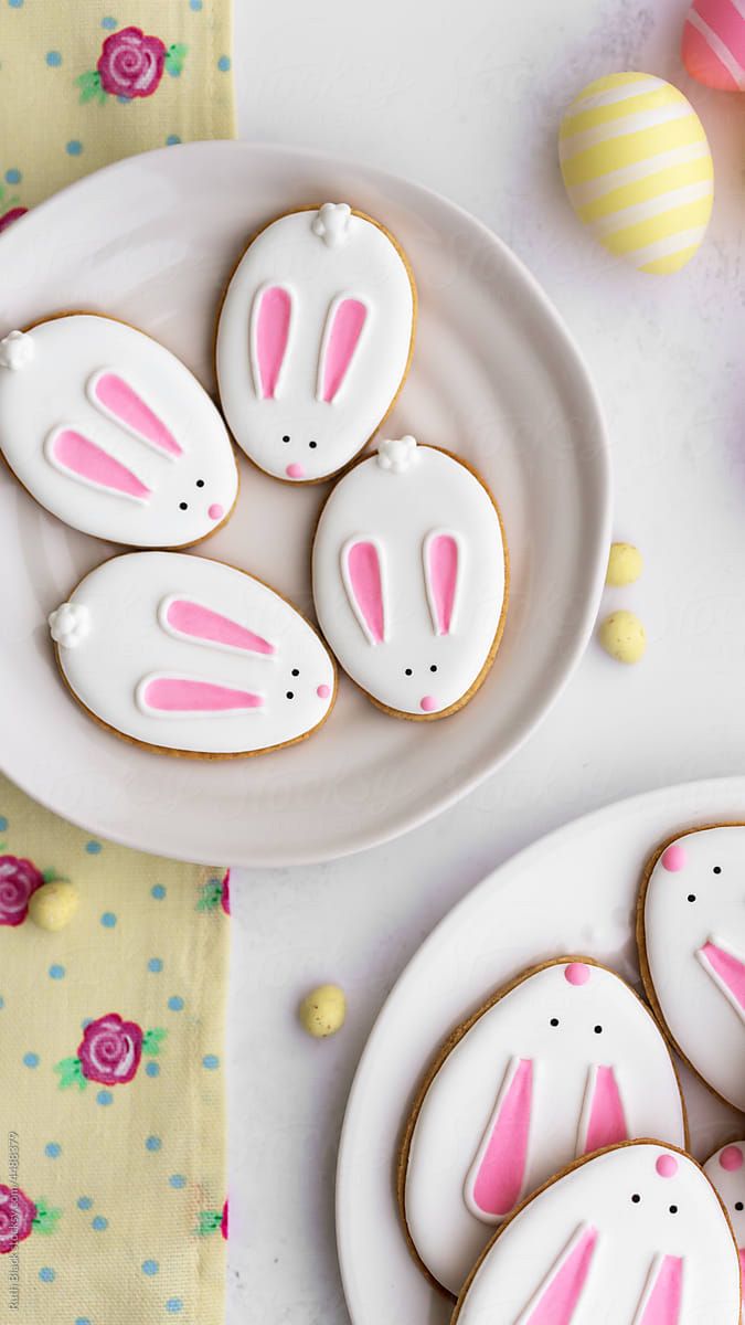 some cookies decorated like bunnies and bunny ears on a white plate next to pink flowers