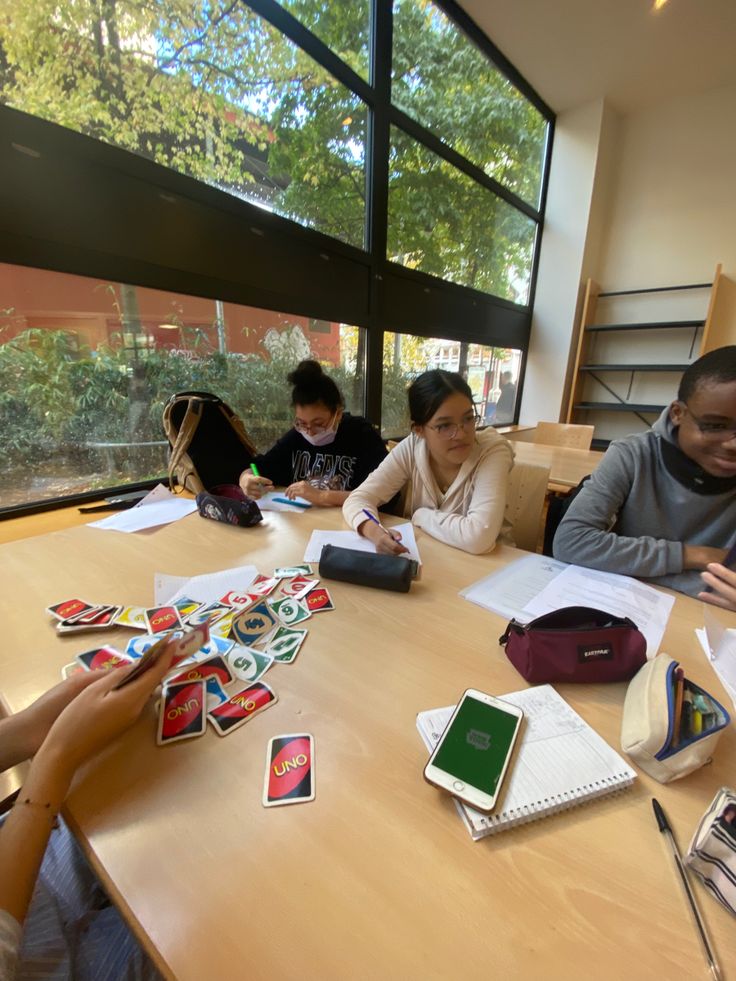 four people sitting at a table with notebooks and papers in front of large windows