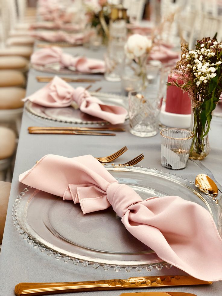 the table is set with pink napkins and gold place settings, along with silverware