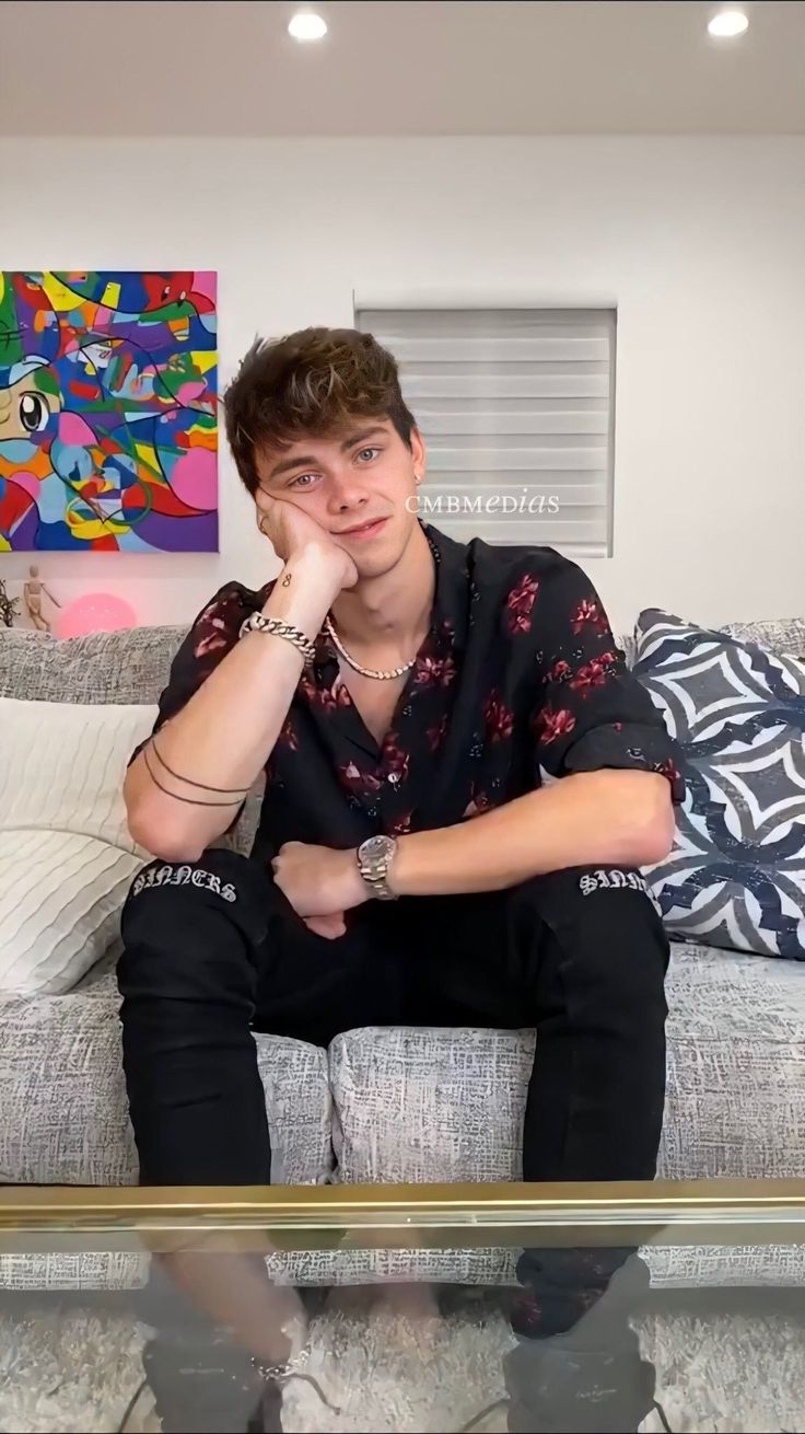 a young man sitting on top of a couch next to a glass topped coffee table