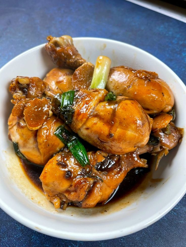 a white bowl filled with meat and vegetables on top of a blue tableclothed surface