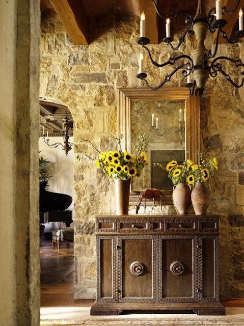 a room with stone walls and a chandelier filled with vases full of sunflowers