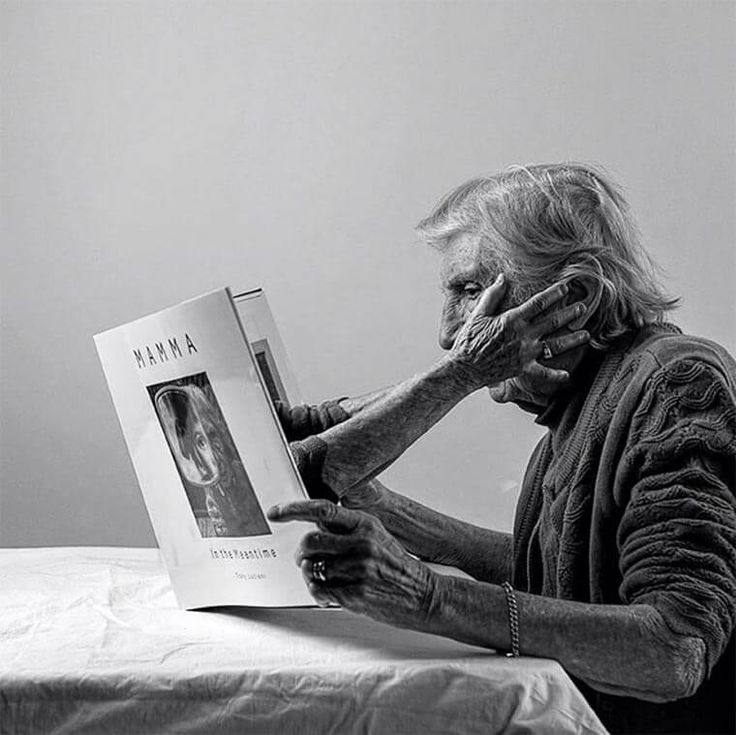 an old woman reading a book while holding her hands to her face in front of her face