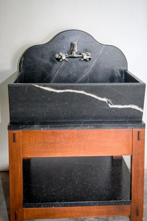 a black marble sink sitting on top of a wooden table next to a white wall