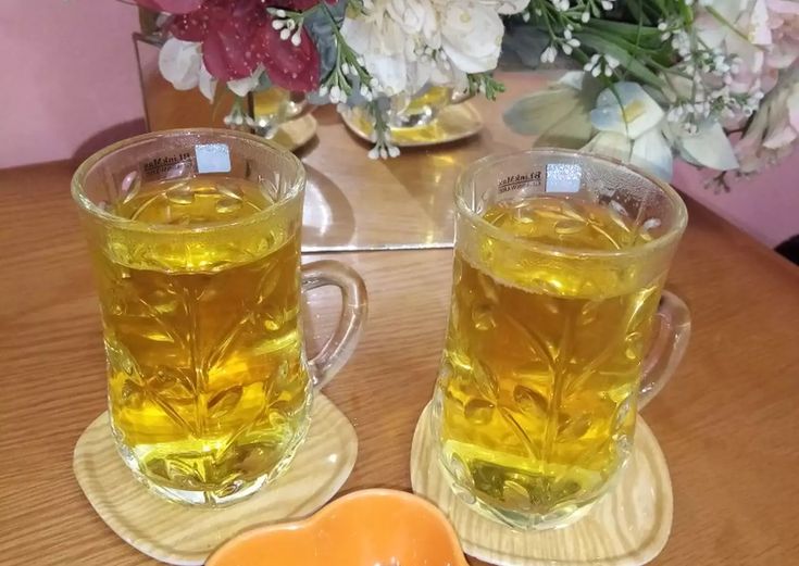 two glasses of tea on a table with flowers in the background