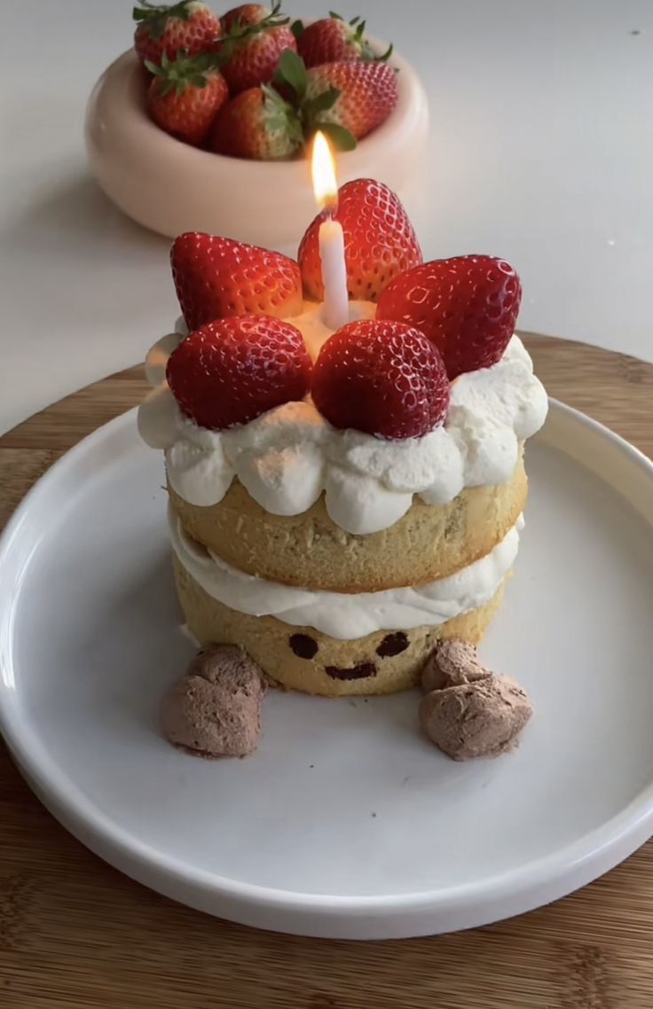 a birthday cake with strawberries on top sitting on a plate next to a bowl of strawberries