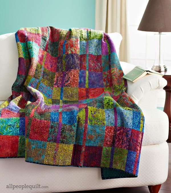 a colorful blanket sitting on top of a white couch next to a lamp in a living room