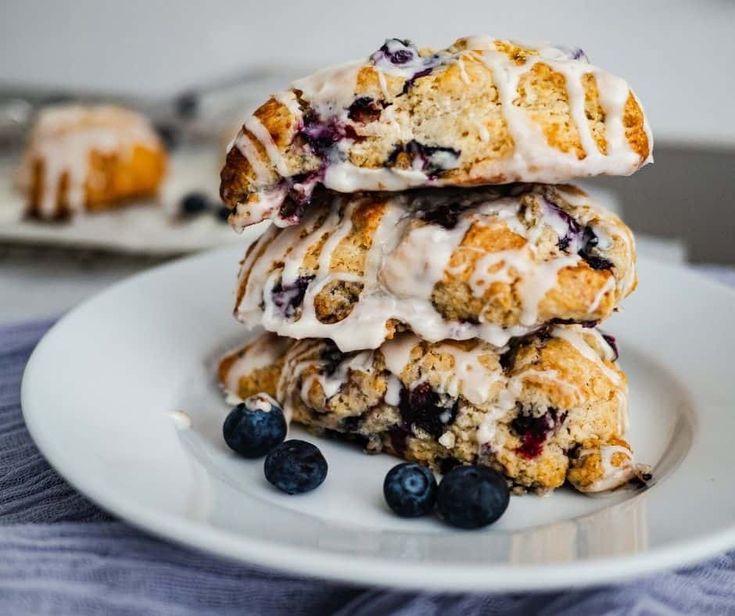 three blueberry scones stacked on top of each other with icing and blueberries